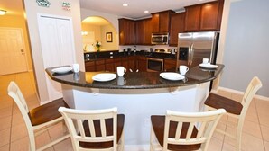 A kitchen with a central island, wooden cabinets, stainless steel appliances, and two white chairs.
