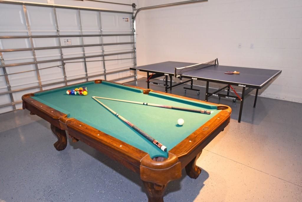 Une table de billard avec des billes et des queues, une table de ping-pong, et une porte de garage en arrière-plan.