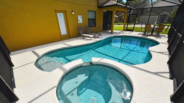 A swimming pool with a circular hot tub, surrounded by lounge chairs and a covered patio area.