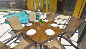 A sunlit outdoor dining area with a pool, yellow walls, and a glass door leading to a covered patio.