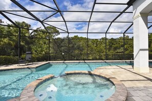 Une piscine intérieure à l’eau claire, entourée d’une structure en verre, et un espace patio avec une chaise.