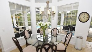 A dining area with a glass table surrounded by chairs, a chandelier, and a clock on the wall.