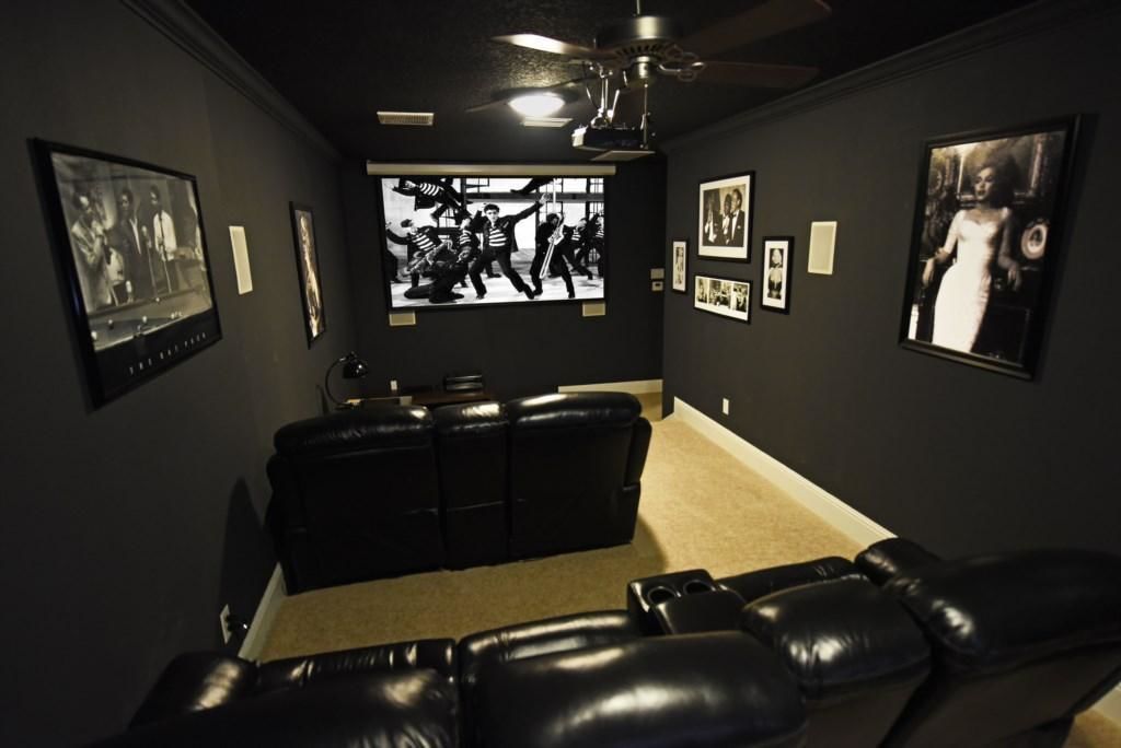 A dark-themed room with a black leather couch, ceiling fan, and wall-mounted artwork.
