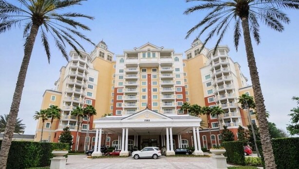A multi-story hotel with a central entrance, surrounded by palm trees and a well-maintained lawn.