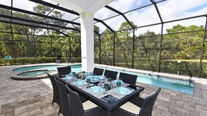 An outdoor pool area with a covered patio, surrounded by lush greenery.