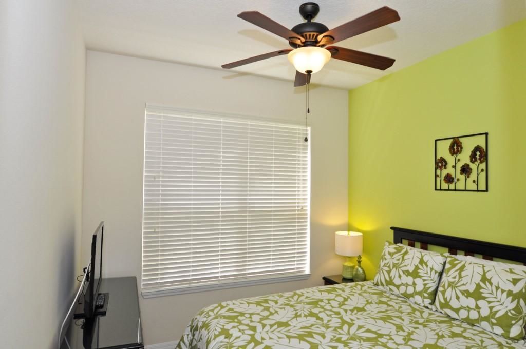 A bedroom with a bed, a ceiling fan, a window with blinds, a bedside lamp, and a wall-mounted picture.