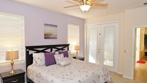 A bedroom with a bed, nightstands, a ceiling fan, and a door leading to another room. - 122 Watersong House 6 Bedroom by Florida Star (Davenport)