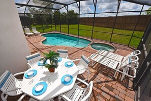 A covered outdoor area with a pool, lounge chairs, and a table set for dining.