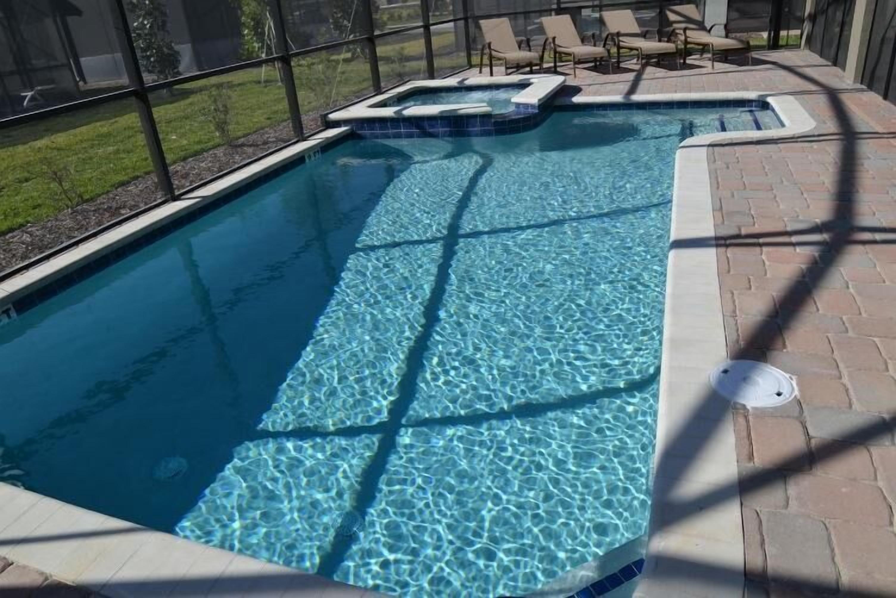 A rectangular swimming pool with clear blue water, surrounded by a brick patio and a glass enclosure.