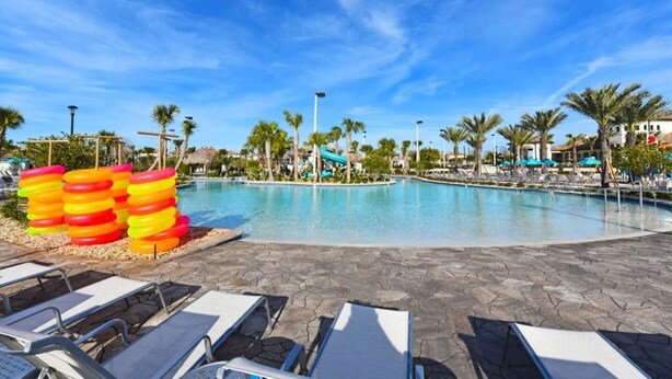 A pool area with lounge chairs, a water slide, palm trees, and a clear blue sky.