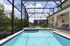 Una piscina con cerramiento de vidrio, rodeada de mobiliario exterior y un porche cubierto.