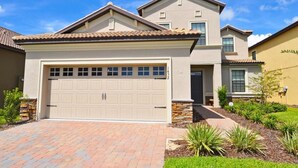 A two-story house with a beige garage door, stone accents, and a well-maintained garden.