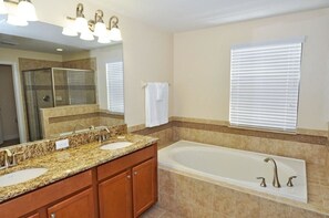 A bathroom with a large mirror, two sinks, a bathtub, and a shower enclosure.