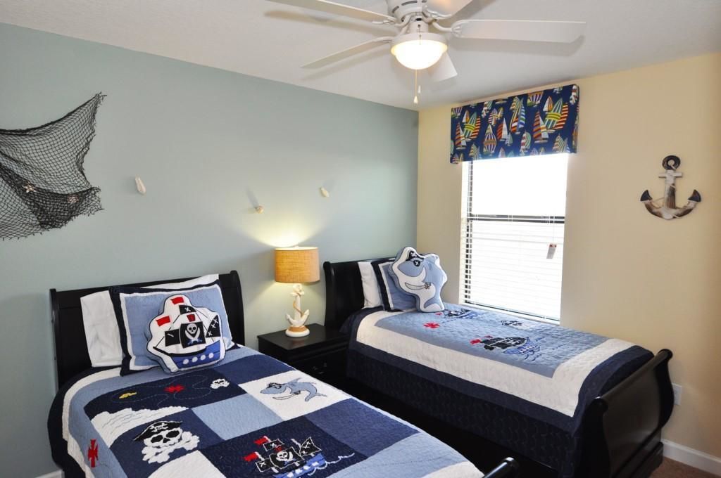 A bedroom with two beds, a ceiling fan, a window with curtains, and a wall decoration.