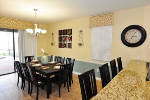 A dining area with a table set for six, surrounded by chairs, a chandelier, and wall-mounted light fixtures. - 1455 Champions House 5 Bedroom by Florida Star (Davenport)