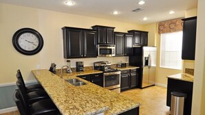 A modern kitchen with granite countertops, black cabinetry, stainless steel appliances, and a clock on the wall.