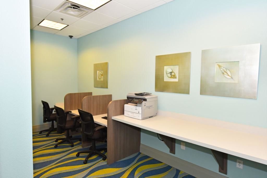 A hotel room with a desk, chairs, and artwork on the walls.