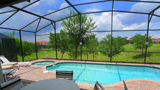 A covered outdoor swimming pool with a patio area, including a table and chairs, and a view of the surrounding landscape.
