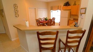 A compact kitchen with a central island, wooden chairs, and a tiled floor.