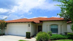 A single-story house with a red-tiled roof, a white garage door, and a small front yard with grass and shrubs.