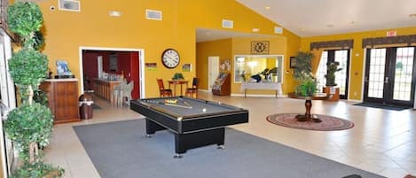 A pool table in a room with yellow walls, a clock, and a door leading to another room.