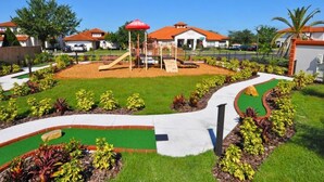 A playground with slides and climbing structures, surrounded by well-maintained lawns and garden beds.