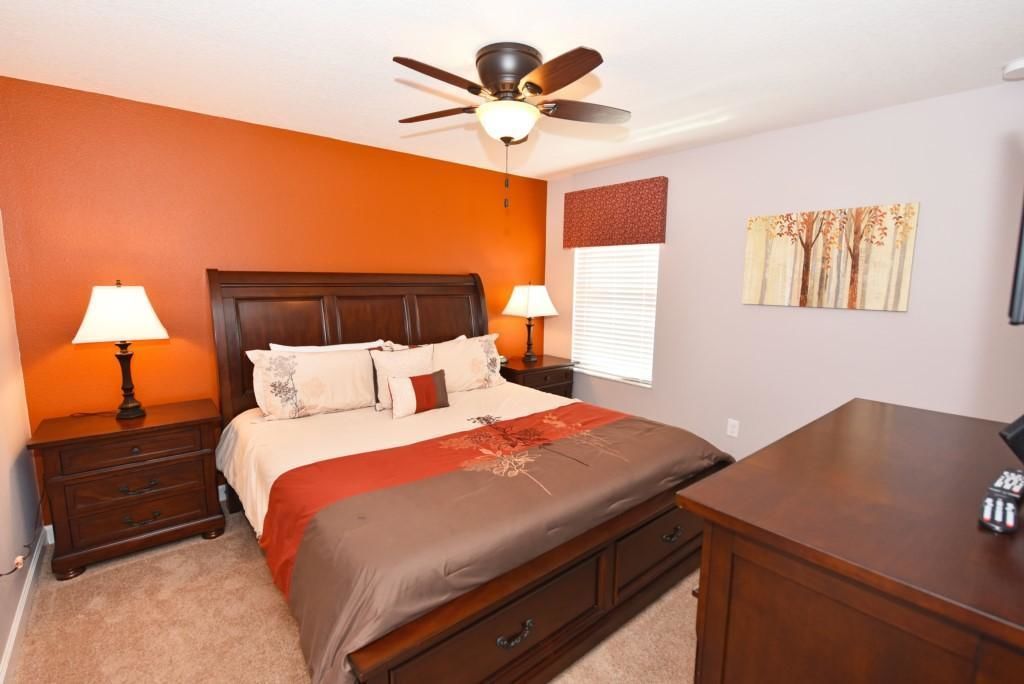 A bedroom with a bed, nightstands, a desk, a ceiling fan, and a window with blinds.