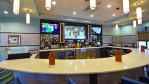 A bar area with a curved counter, multiple screens displaying content, and overhead lighting fixtures. - 1490 Champions House 8 Bedroom by Florida Star (Davenport)