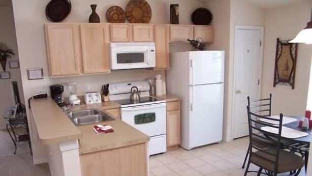 A compact kitchen with a microwave, stove, refrigerator, and a dining area with a table and chairs. - 157 Sandy Ridge House 5 Bedroom by Florida Star (Davenport)