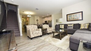 A living room with a sofa, armchairs, a coffee table, and a staircase.