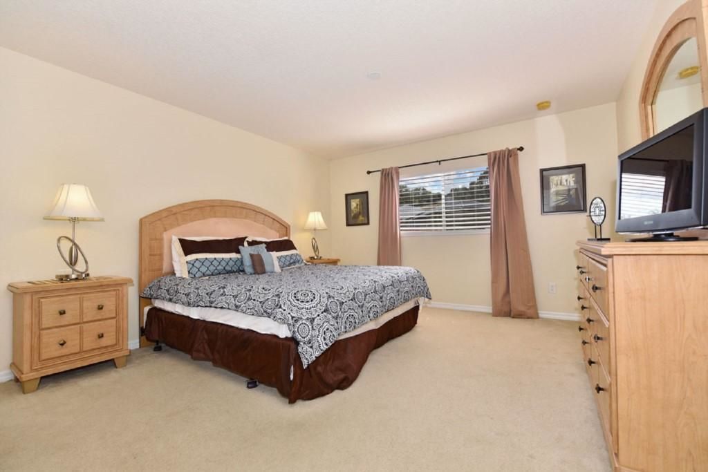 A bedroom with a bed, a dresser, a television, and a window with curtains.