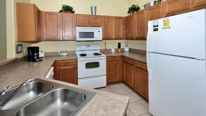 A kitchen with wooden cabinets, a white stove, a microwave, and a refrigerator.