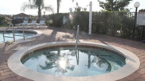 A swimming pool with a brick border, surrounded by lounge chairs and a fence.