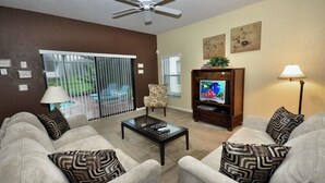A living room with a ceiling fan, a television, a coffee table, and two sofas with patterned cushions.