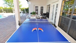 A ping pong table with two paddles in the center, surrounded by outdoor seating and a pool.