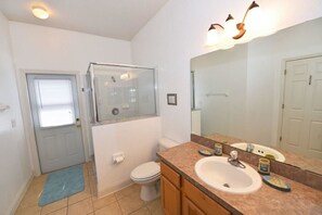 A bathroom with a glass shower enclosure, a white toilet, a sink with a mirror, and a blue mat on the floor. - 16659 High Grove House 3 Bedroom by Florida Star (Clermont)