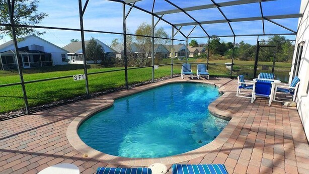 A covered swimming pool with blue chairs and a small table. - 16708 High Grove House 4 Bedroom by Florida Star (Clermont)