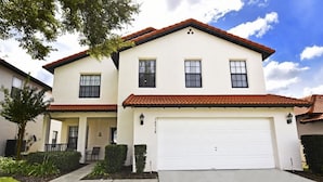 A two-story house with a white exterior, a red-tiled roof, and a white garage door. - 16718 High Grove House 4 Bedroom by Florida Star (Clermont)