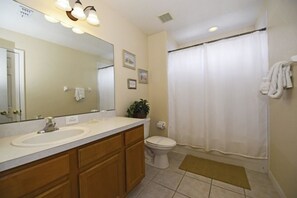 A bathroom with a sink, mirror, toilet, and shower curtain.