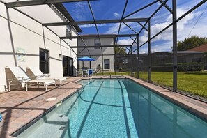 A swimming pool with a covered area, lounge chairs, and a blue umbrella.