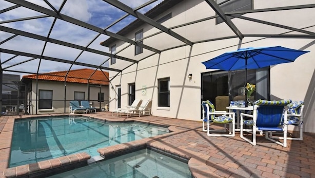 An indoor swimming pool with a glass ceiling, surrounded by lounge chairs and a blue umbrella. - 16718 High Grove House 4 Bedroom by Florida Star (Clermont)