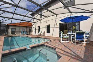 An indoor swimming pool with a glass ceiling, surrounded by lounge chairs and a blue umbrella.