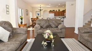 A living room with two sofas, a coffee table with decorative items, and a view into the kitchen area. - 16718 High Grove House 4 Bedroom by Florida Star (Clermont)