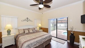 A bedroom with a bed, two bedside lamps, a ceiling fan, a sliding glass door to a patio, and a TV on the wall. - 16805 High Grove House 4 Bedroom by Florida Star (Clermont)
