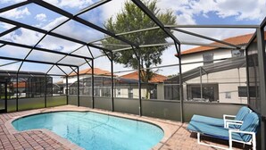 A covered swimming pool with a brick border, a lounge chair, and a view of houses in the background. - 16805 High Grove House 4 Bedroom by Florida Star (Clermont)