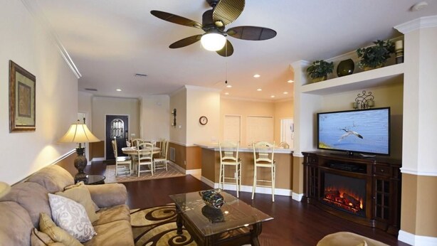 A living room with a sofa, coffee table, TV, fireplace, and a ceiling fan. - 16805 High Grove House 4 Bedroom by Florida Star (Clermont)
