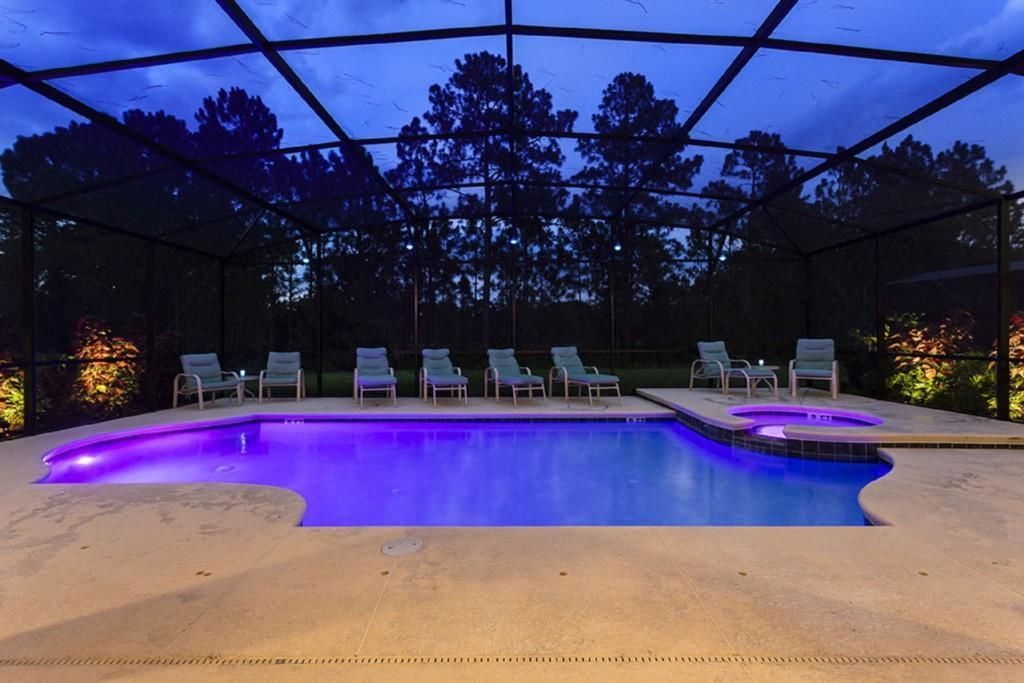 A swimming pool with a glass enclosure, surrounded by lounge chairs and a hot tub.