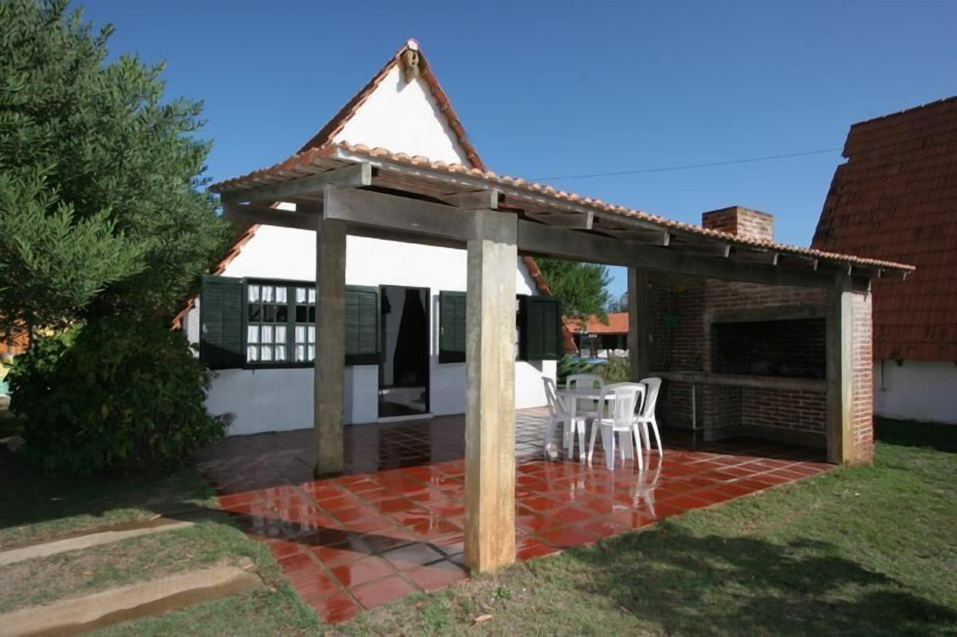 A covered patio with a tiled floor, a brick barbecue area, and a white building with a tiled roof.
