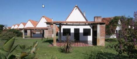 Uma fileira de edifícios brancos com telhados de telha vermelha, cercada por vegetação.