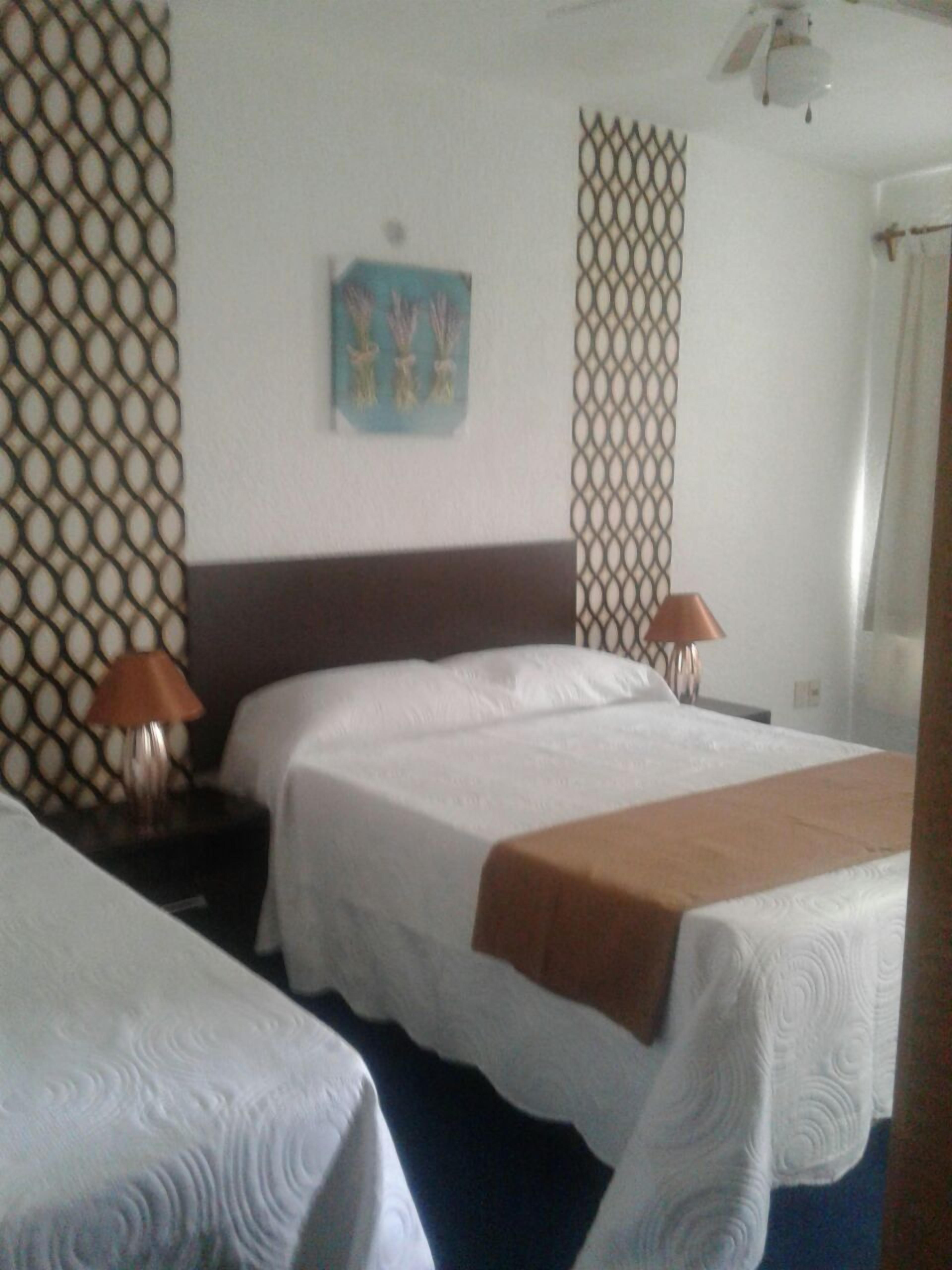 A hotel room with two beds, a nightstand with a lamp, a decorative wall panel, and a painting.